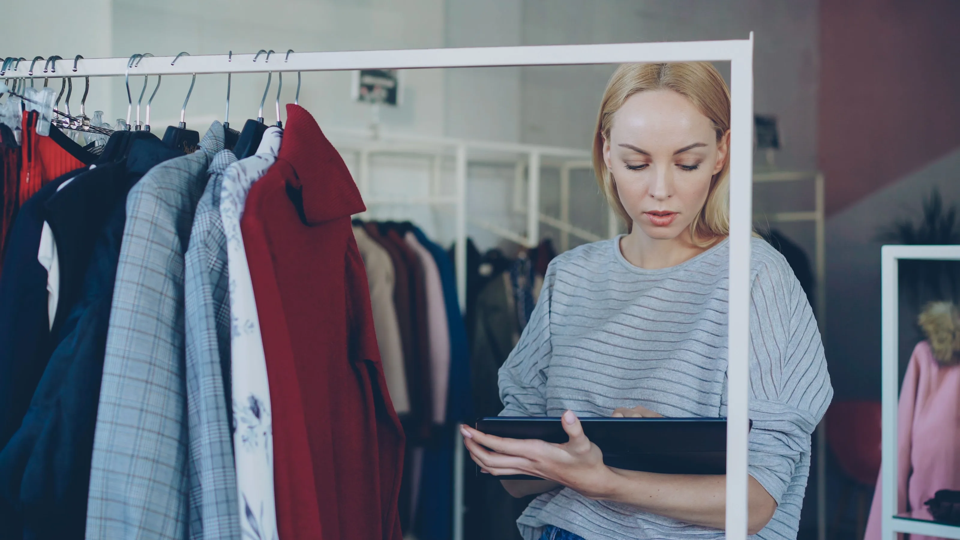 Una empleada revisa una tableta entre los percheros de una tienda de ropa